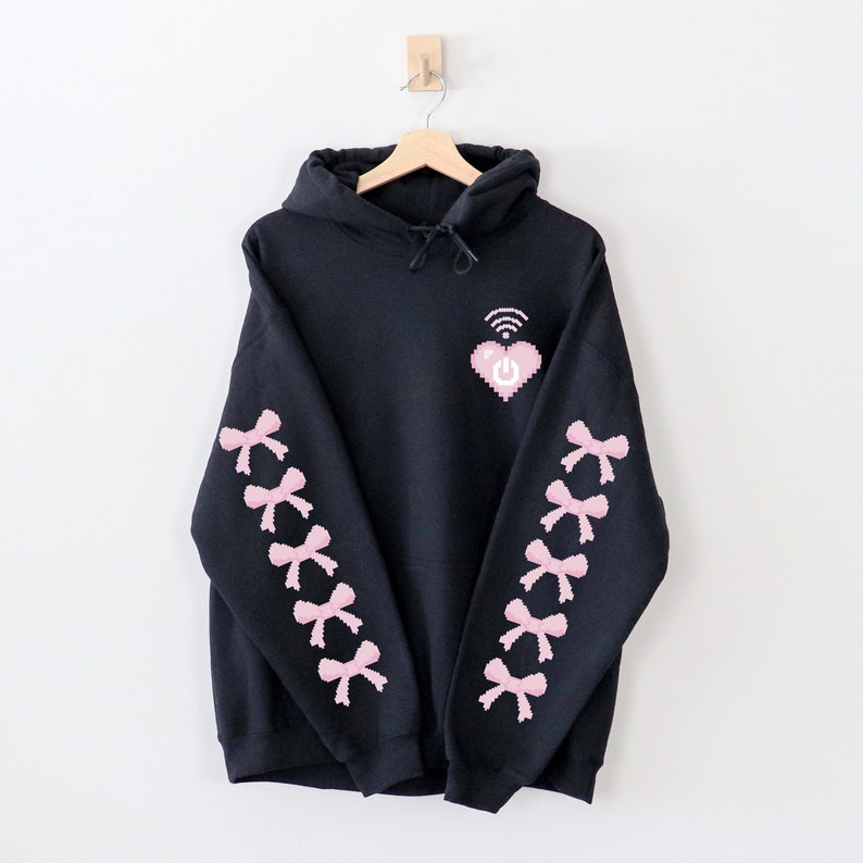 May include: Black hoodie with a pink pixelated heart with a wifi symbol and power button on the front. The sleeves have pink pixelated bows.