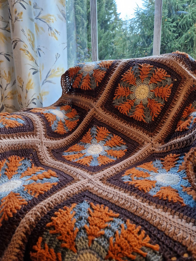 May include: A crocheted throw blanket with a brown, orange, and blue geometric pattern. The blanket is made of soft yarn and has a textured surface.
