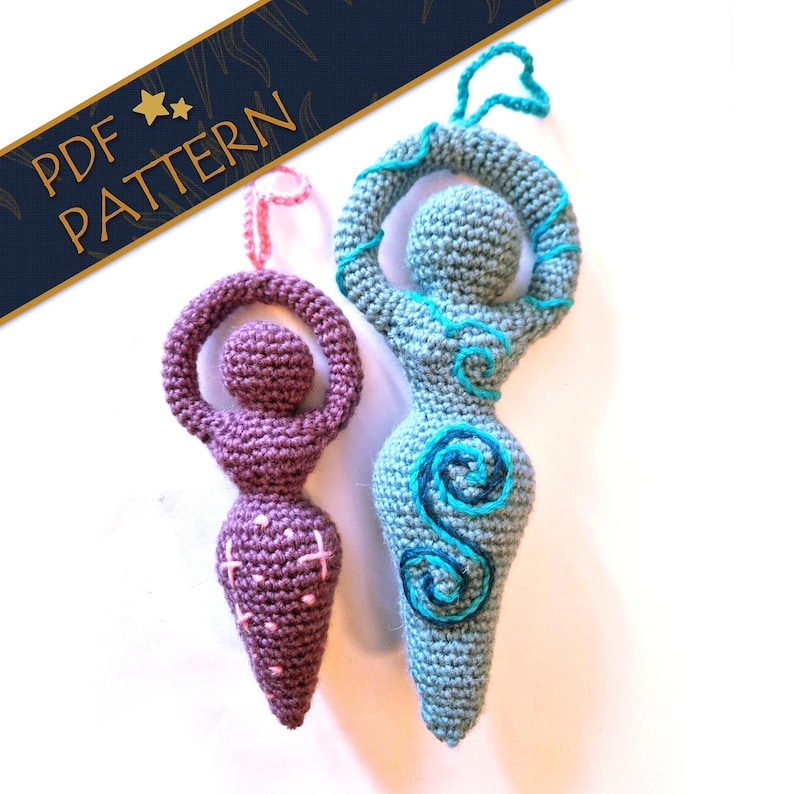 May include: Two crocheted goddess figures with hanging loops. The smaller figure is purple with pink embroidered star accents. The larger figure is light blue with dark blue and teal embroidered spiral patterns. A banner reads PDF PATTERN.