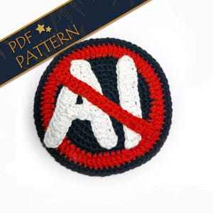 Puede incluir: Un parche de ganchillo con fondo negro, borde rojo y símbolo "IA" blanco tachado con una línea roja. El parche es redondo y tiene el texto "PDF PATTERN" en una pancarta azul.