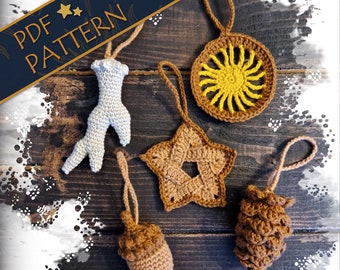 May include: Five crocheted ornaments in various shapes and colors, including a star, a sun, a pinecone, an acorn, and a twig. The ornaments are brown, yellow, and white and are hanging from a wooden surface.
