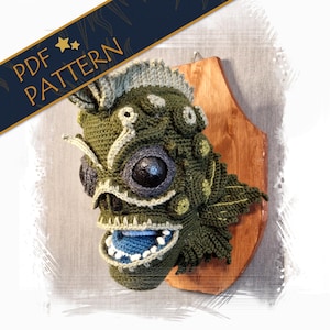 May include: A crocheted green monster head with a toothy grin, large eyes, and a spiky crest. The head is mounted on a wooden plaque.