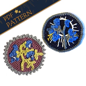 Könnte beinhalten: Zwei gehäkelte Blumenmotive, eines mit dunkelblauem Hintergrund und das andere mit burgunderfarbenem Hintergrund. Beide Motive zeigen blaue Blumen mit gelben Stielen.