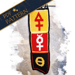 May include: A crocheted wall hanging with three panels. The top panel is yellow with a white symbol, the middle panel is red with a white symbol, and the bottom panel is black with a gold symbol.