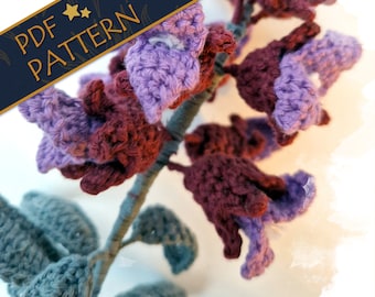 Puede incluir: Patrón de ganchillo para una flor morada y burdeos con hojas verdes. El patrón está disponible para descargar en PDF.