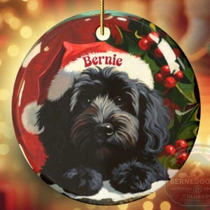 A black bernedoodle dog wearing a santa hat that is personalized with their name on it in this adorable Ceramic ornament!