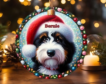 Könnte beinhalten: Runder Weihnachtsschmuck mit einem Bernedoodle-Hund mit Weihnachtsmütze. Der Schmuck hat einen festlichen Rand mit bunten Lichtern und dem Namen "Bernie" in Rot. Zum Aufhängen ist eine braune Schnur befestigt.