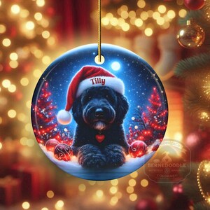 This festive ornament features an adorable black doodle wearing a Santa hat, surrounded by soft glowing holiday lights and rich red Christmas tones. The warm lighting highlights the dog’s fluffy black fur, giving the design a bright, cheerful look that stands out on any tree. A perfect personalized keepsake for anyone who loves black doodles and joyful holiday décor.