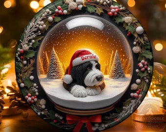 Könnte beinhalten: Runder Weihnachtsschmuck mit Schneekugel-Design. Im Inneren befindet sich ein schwarz-weißer Hund mit Weihnachtsmütze und dem Namen "Bernie" in einer verschneiten Szene mit Tannen. Der Schmuck ist mit Stechpalmen und Beeren verziert.