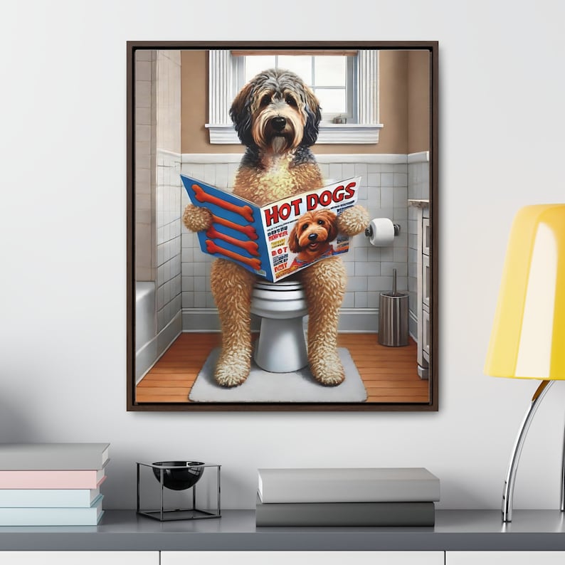 May include: A framed canvas art piece featuring a dog sitting on a toilet, reading a magazine titled 'Hot Dogs.' The dog is brown and tan with a fluffy coat. The magazine cover shows a dog. The bathroom has a window, a toilet paper roll, and a white bathtub.