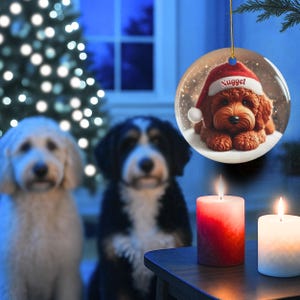 This ceramic ornament features a cute red mini-doodle golden doodle or goldendoodle dog wearing a Santa hat in a snow globe setting, surrounded by holiday decorations. Perfect for adding a festive touch to your Christmas tree or as a thoughtful gift for dog lovers.
