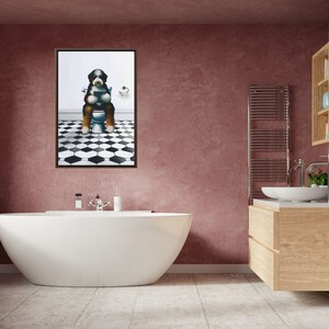 May include: A framed wall art print featuring a Bernese Mountain Dog sitting on a white toilet while reading a book. The dog has black, white, and brown fur. The background shows a white wall and a floor with a black and white hexagonal tile pattern.
