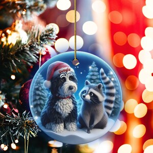 A 3-inch double-sided ceramic Christmas ornament featuring an adorable claymation-style Bernedoodle wearing a red Santa hat personalized  sitting beside a cute raccoon under a snowy winter night sky. The ornament has crisp detailing, soft blue tones, and a warm Christmas glow in the blurred background. Perfect for Bernedoodle lovers, handmade Christmas gift shoppers. High-quality ceramic with vibrant colors, ideal for tree decorating, pet memorial ornaments, or festive seasonal displays.