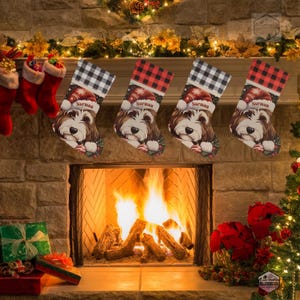 A festive Christmas stocking featuring a whimsical illustrated doodle dog wearing a red Santa hat, surrounded by holiday ornaments and greenery in a warm, detailed Christmas art style. The top of the stocking has a classic red and black buffalo-plaid cuff, and the stocking hangs from a white mantel decorated with evergreen garland and gold ornaments. The stocking design is personalized with your dog’s name, making it a charming and custom holiday décor piece for dog lovers.
