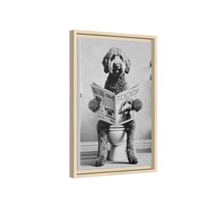 May include: A black and white framed wall art print featuring a curly-haired dog sitting on a toilet while reading a newspaper titled DOG. The dog has shaggy fur and is holding the open newspaper with both front paws in a vertical orientation.