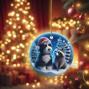 A 3-inch double-sided ceramic Christmas ornament featuring an adorable claymation-style Bernedoodle wearing a red Santa hat personalized  sitting beside a cute raccoon under a snowy winter night sky. The ornament has crisp detailing, soft blue tones, and a warm Christmas glow in the blurred background. Perfect for Bernedoodle lovers, handmade Christmas gift shoppers. High-quality ceramic with vibrant colors, ideal for tree decorating, pet memorial ornaments, or festive seasonal displays.