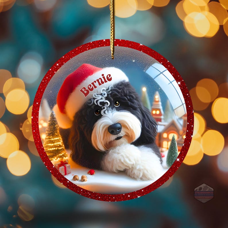K&ouml;nnte beinhalten: Ein runder Weihnachtsschmuck mit rotem Glitzerrahmen. Im Inneren befindet sich ein schwarz-wei&szlig;er Hund mit Weihnachtsm&uuml;tze und dem Namen "Bernie" vor einer Winterlandschaft. Der Hintergrund zeigt eine verschneite Landschaft und ein kleines Dorf.