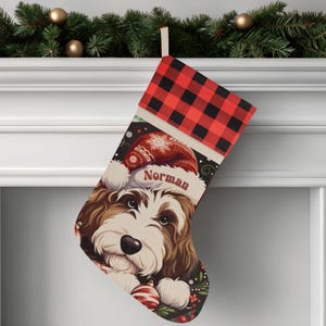 A festive Christmas stocking featuring a whimsical illustrated doodle dog wearing a red Santa hat, surrounded by holiday ornaments and greenery in a warm, detailed Christmas art style. The top of the stocking has a classic red and black buffalo-plaid cuff, and the stocking hangs from a white mantel decorated with evergreen garland and gold ornaments. The stocking design is personalized with your dog’s name, making it a charming and custom holiday décor piece for dog lovers.