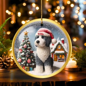 May include: A circular Christmas decoration with a gold edge. It features a dog wearing a Santa hat in a snowy scene with a Christmas tree and a house. The dog's name, "Willis", is printed on the hat.