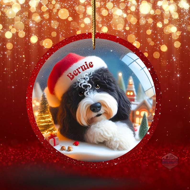 K&ouml;nnte beinhalten: Ein runder Weihnachtsschmuck mit einem schwarz-wei&szlig;en Hund, der einen Weihnachtsmannhut mit dem Namen "Bernie" tr&auml;gt. Der Schmuck hat einen roten Rand und einen goldenen Faden zum Aufh&auml;ngen. Der Hintergrund zeigt eine verschneite Szene.