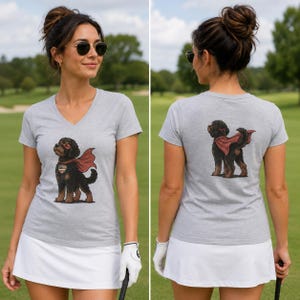 May include: A heather gray V-neck t-shirt featuring a graphic of a black curly-haired dog wearing a red superhero cape and mask. The front graphic includes a heart-shaped tag, while the back graphic shows the dog from behind in the same cape.