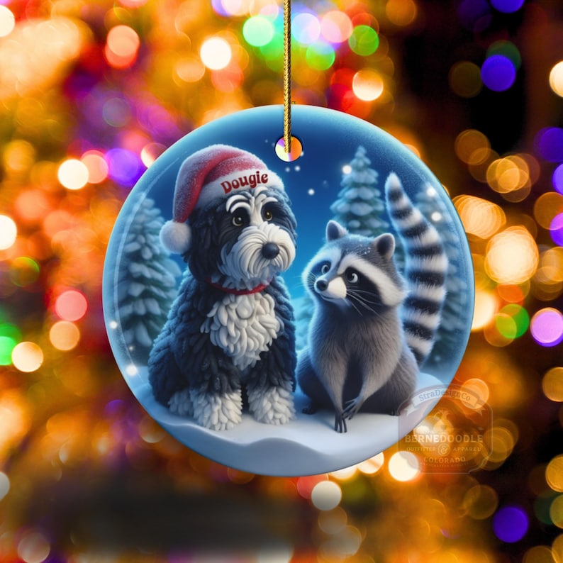 A 3-inch double-sided ceramic Christmas ornament featuring an adorable claymation-style Bernedoodle wearing a red Santa hat personalized  sitting beside a cute raccoon under a snowy winter night sky. The ornament has crisp detailing, soft blue tones, and a warm Christmas glow in the blurred background. Perfect for Bernedoodle lovers, handmade Christmas gift shoppers. High-quality ceramic with vibrant colors, ideal for tree decorating, pet memorial ornaments, or festive seasonal displays.