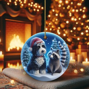A 3-inch double-sided ceramic Christmas ornament featuring an adorable claymation-style Bernedoodle wearing a red Santa hat personalized  sitting beside a cute raccoon under a snowy winter night sky. The ornament has crisp detailing, soft blue tones, and a warm Christmas glow in the blurred background. Perfect for Bernedoodle lovers, handmade Christmas gift shoppers. High-quality ceramic with vibrant colors, ideal for tree decorating, pet memorial ornaments, or festive seasonal displays.