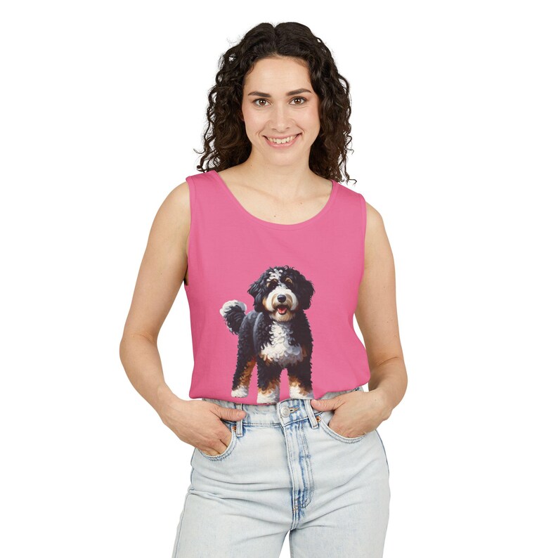 May include: A sleeveless pink tank top featuring a Bernese Mountain Dog illustration. The dog is depicted in black, white, and brown, with a fluffy tail and a happy expression. The tank top is made of a soft material.
