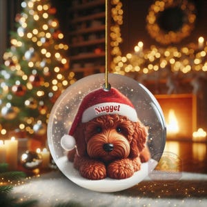 This ceramic ornament features a cute red mini-doodle golden doodle or goldendoodle dog wearing a Santa hat in a snow globe setting, surrounded by holiday decorations. Perfect for adding a festive touch to your Christmas tree or as a thoughtful gift for dog lovers.
