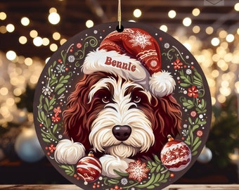 May include: Round Christmas ornament featuring a dog wearing a Santa hat with the name "Bennie". The ornament has a brown background with a decorative floral border and two red and white ornaments. A gold string is attached for hanging.