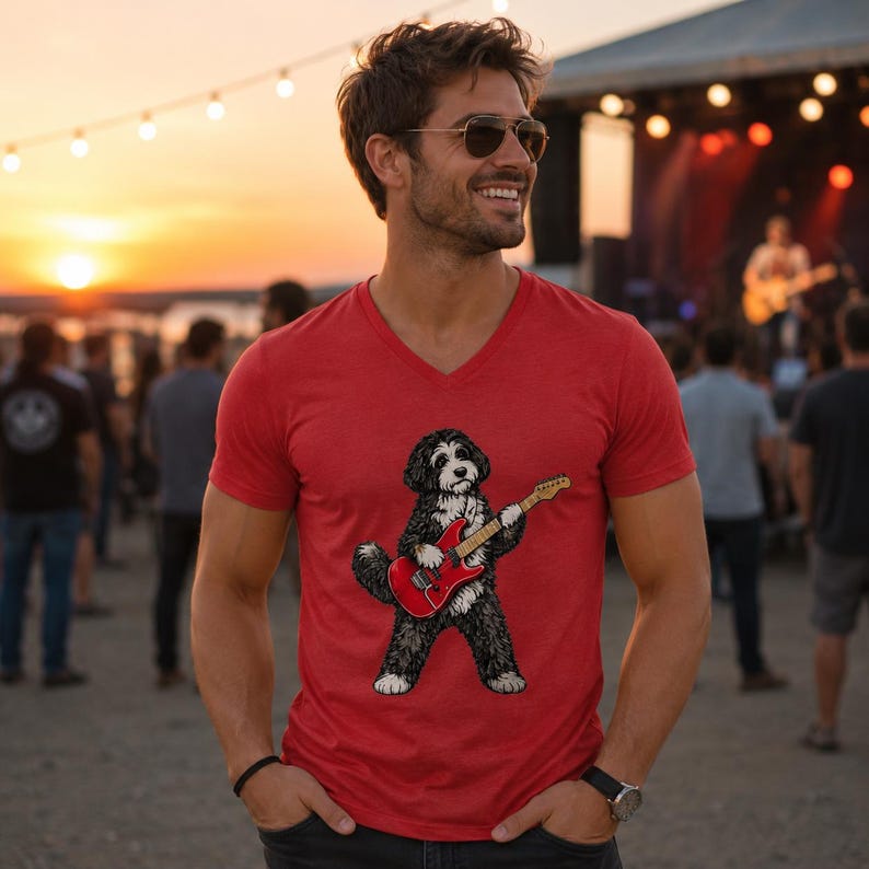 May include: A red V-neck t-shirt featuring a graphic illustration of a black and white dog playing a red electric guitar. The shirt has short sleeves and a standard fit, showcasing a detailed print of the canine musician centered on the chest.