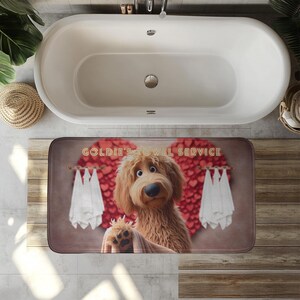 A cute golden doodle stands in front of a fluffy red heart backdrop, holding a brown towel on a cozy bath mat. White towels hang on either side, creating a spa-like feel. The text “Goldie’s Towel Service” sits above the doodle. Perfect for dog lovers, bathroom décor, and pet-themed home accents.