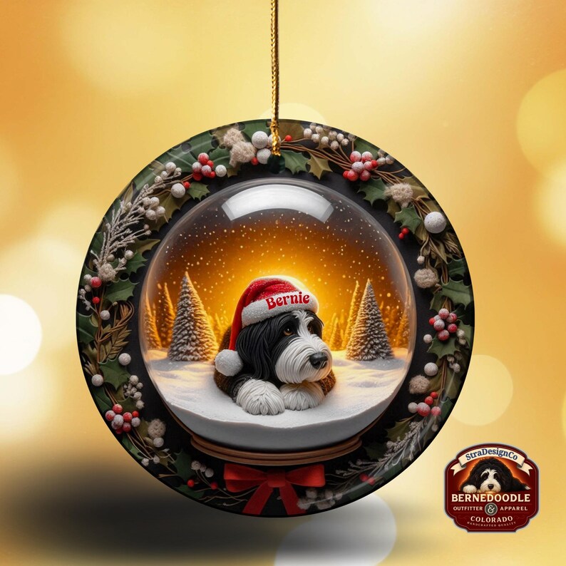 May include: A round Christmas ornament featuring a Bernedoodle dog inside a snow globe. The dog wears a Santa hat with the name "Bernie". The ornament is decorated with holly and berries, and has a red bow at the bottom.