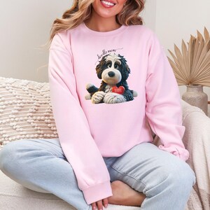 A woman wearing a Bernedoodle sweatshirt with cute design on the front and the back.  The front features a bernedoodle dog in claymation design holding a heart with his name, across the top of his head the words, "Doodle Mom".