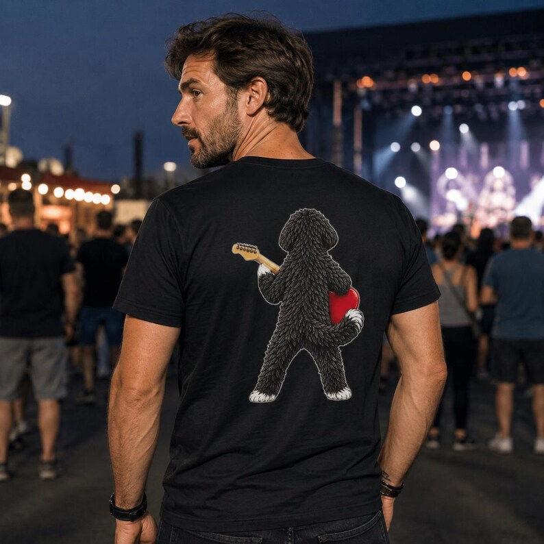 May include: A black short-sleeved t-shirt featuring a graphic on the back of a fluffy black dog standing on its hind legs, holding a light-colored electric guitar and a bright red heart shape against its side, viewed from the back.