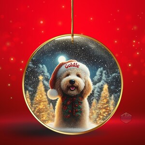 May include: A Christmas ornament featuring a fluffy dog wearing a Santa hat with the name "Goldie" and a festive scarf. The dog is set against a snowy winter scene with Christmas trees and a full moon, all within a gold-rimmed glass ball.