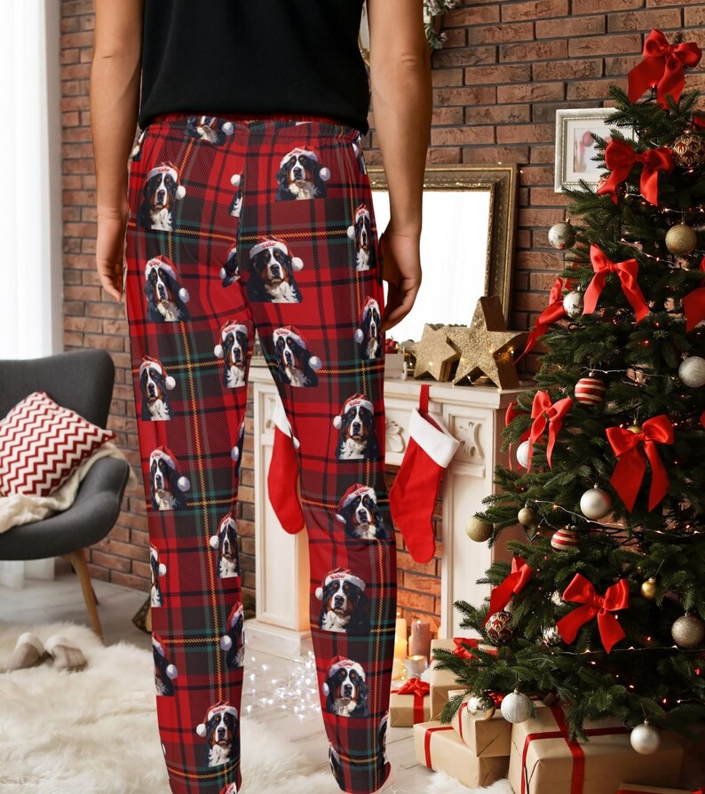 A man seen wearing Men's pajama pants lounge wear personalized Christmas pajama bottoms with Bernese Mountain dogs wearing Santa Hat and their name is on the Santa Hat.  Bernese Mountain Dog dad gear!