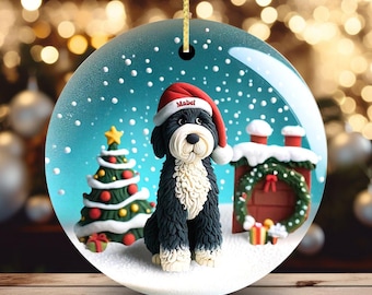 May include: A round Christmas ornament featuring a black and white dog wearing a Santa hat with the name "Mabel". The ornament has a winter scene with a Christmas tree, snow, and a decorated chimney.