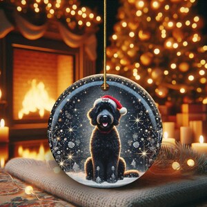 May include: Round Christmas ornament featuring a black dog wearing a Santa hat, set against a snowy winter scene with sparkling lights. The ornament has a gold string for hanging and is perfect for holiday decor.
