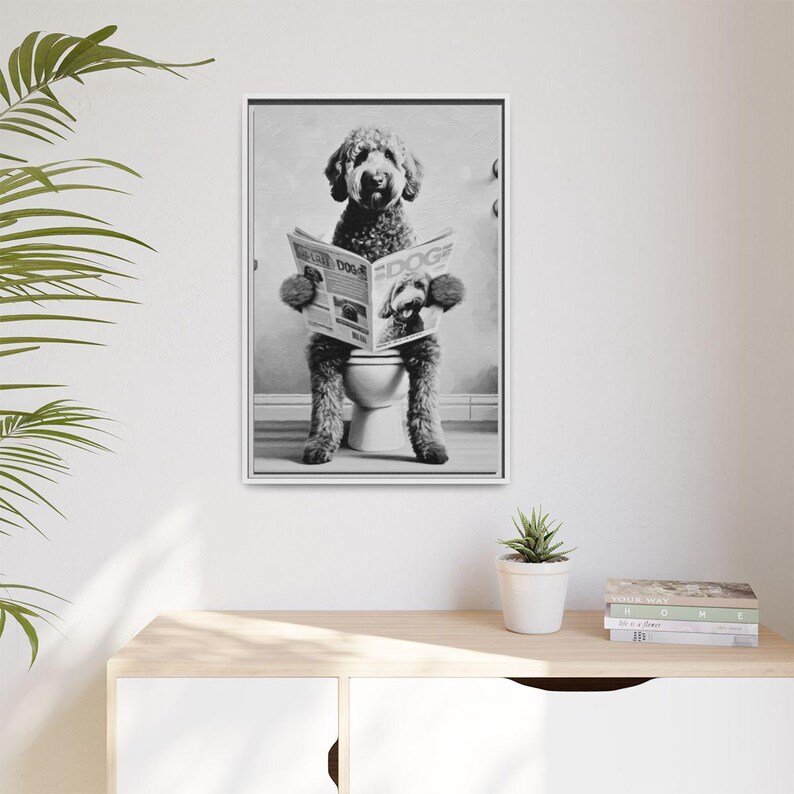 May include: A black and white framed wall art print depicting a curly-haired dog sitting on a toilet while reading a newspaper titled The Daily Dog. The dog is positioned upright, holding the open newspaper with its front paws in a humorous pose.