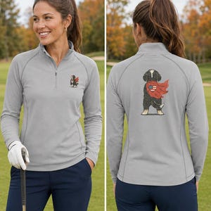 K&ouml;nnte beinhalten: Ein hellgrauer Langarm-Pullover mit kurzem Rei&szlig;verschluss, der auf der linken Brust ein kleines Motiv eines schwarz-wei&szlig;en Hundes mit rotem Umhang zeigt, sowie eine gr&ouml;&szlig;ere Version desselben Hundemotivs auf der R&uuml;ckseite zwischen den Schulterbl&auml;ttern.