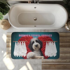 May include: A rectangular bath mat featuring a dog with black and white fur, towels, and the text "BERNIE'S TOWEL SERVICE". The dog is positioned in front of a red heart-shaped design, with white towels hanging on wooden rods.