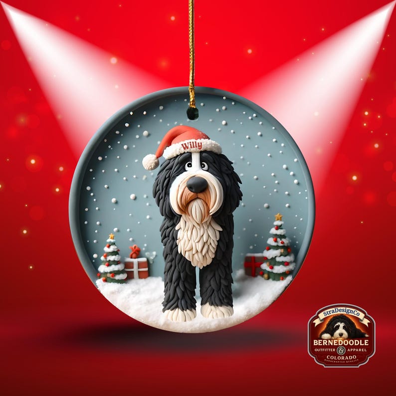 May include: A round Christmas ornament featuring a Bernedoodle dog wearing a Santa hat with the name "Willy". The ornament has a snowy scene with Christmas trees and gifts. The ornament is hanging from a gold string.