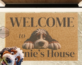 May include: A rectangular doormat with the words "WELCOME to Bonnie's House" in dark brown lettering. The mat features a graphic of a dog with a sad expression. The mat is made of a light brown material.