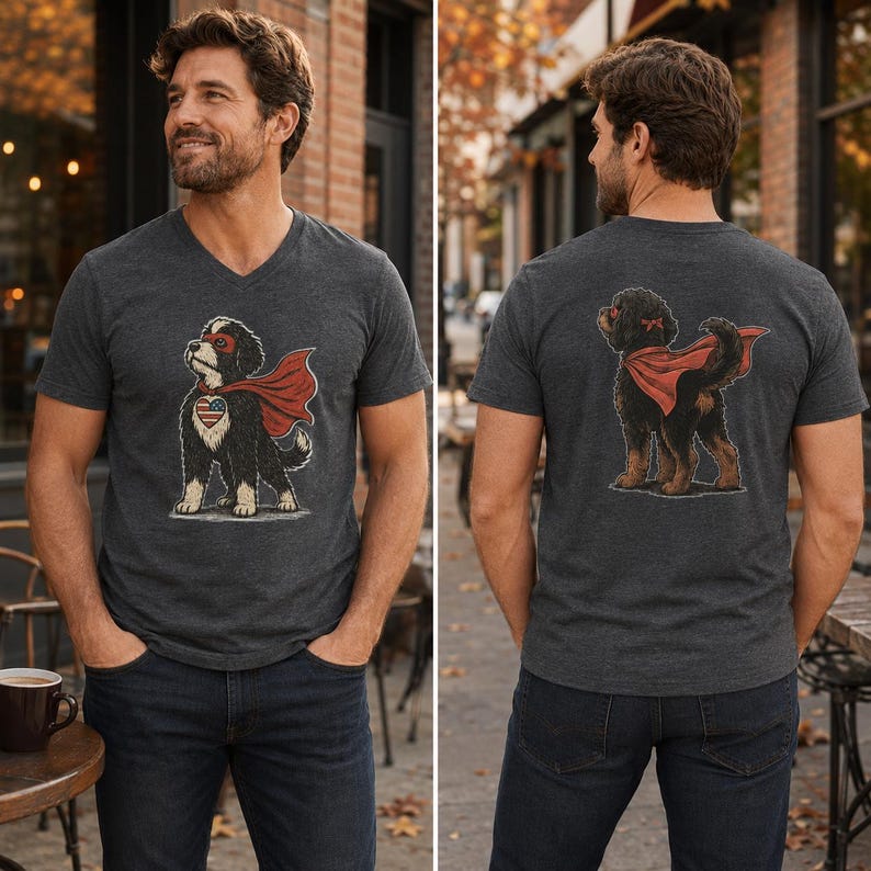 May include: A charcoal grey V-neck t-shirt featuring a graphic of a black and white dog wearing a red superhero cape and mask. The front graphic shows the dog with a heart-shaped American flag patch, while the back graphic shows the dog from behind.