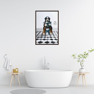 May include: A framed wall art print featuring a black, white, and brown dog sitting on a white toilet in a bathroom with a black and white hexagonal tiled floor. The dog is holding a dark rectangular object in its front paws while sitting upright.