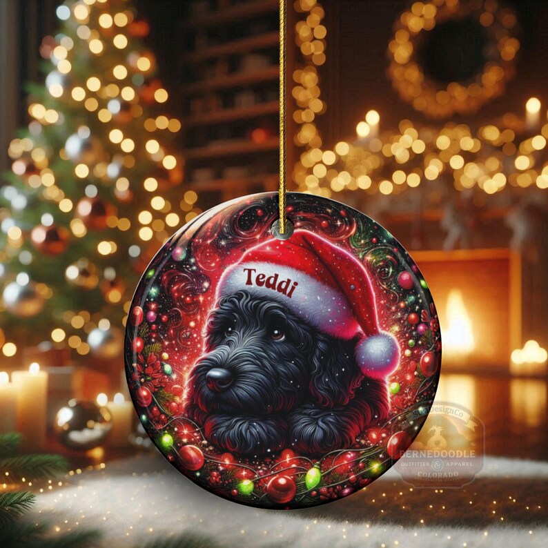 May include: A round Christmas ornament featuring a black dog wearing a red Santa hat with the name "Teddi" on it. The ornament is decorated with Christmas lights and festive colors, perfect for holiday decor.
