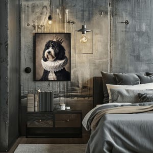 May include: A framed portrait of a black and white dog wearing a crown and ruffled collar hangs above a nightstand in a bedroom. The nightstand has two drawers and a stack of books. A bed with gray bedding is in the foreground.