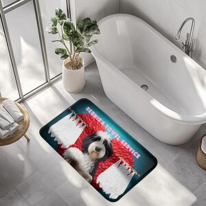May include: A rectangular bath mat featuring a black and white dog with the text "BERNIE'S TOWEL SERVICE". The mat has a teal background with red and white accents, and is placed in a bathroom setting.