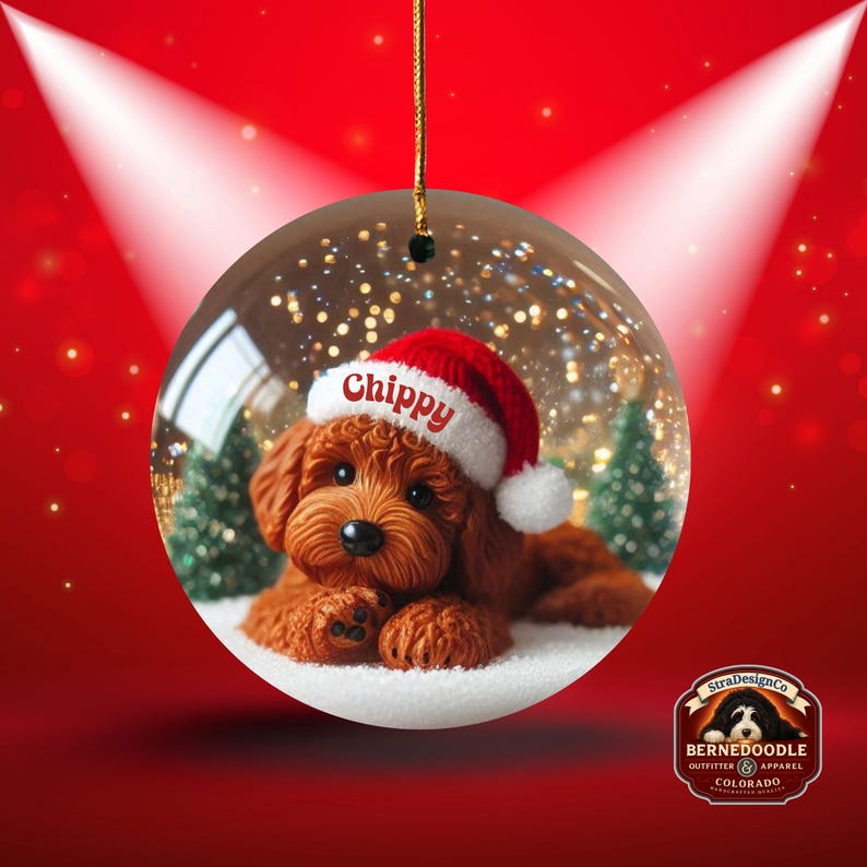 May include: A clear glass Christmas bauble featuring a brown dog wearing a Santa hat with the name "Chippy" on it. The bauble has a gold string for hanging and is set against a red background with a spotlight effect. The bauble also has a snow-like base.